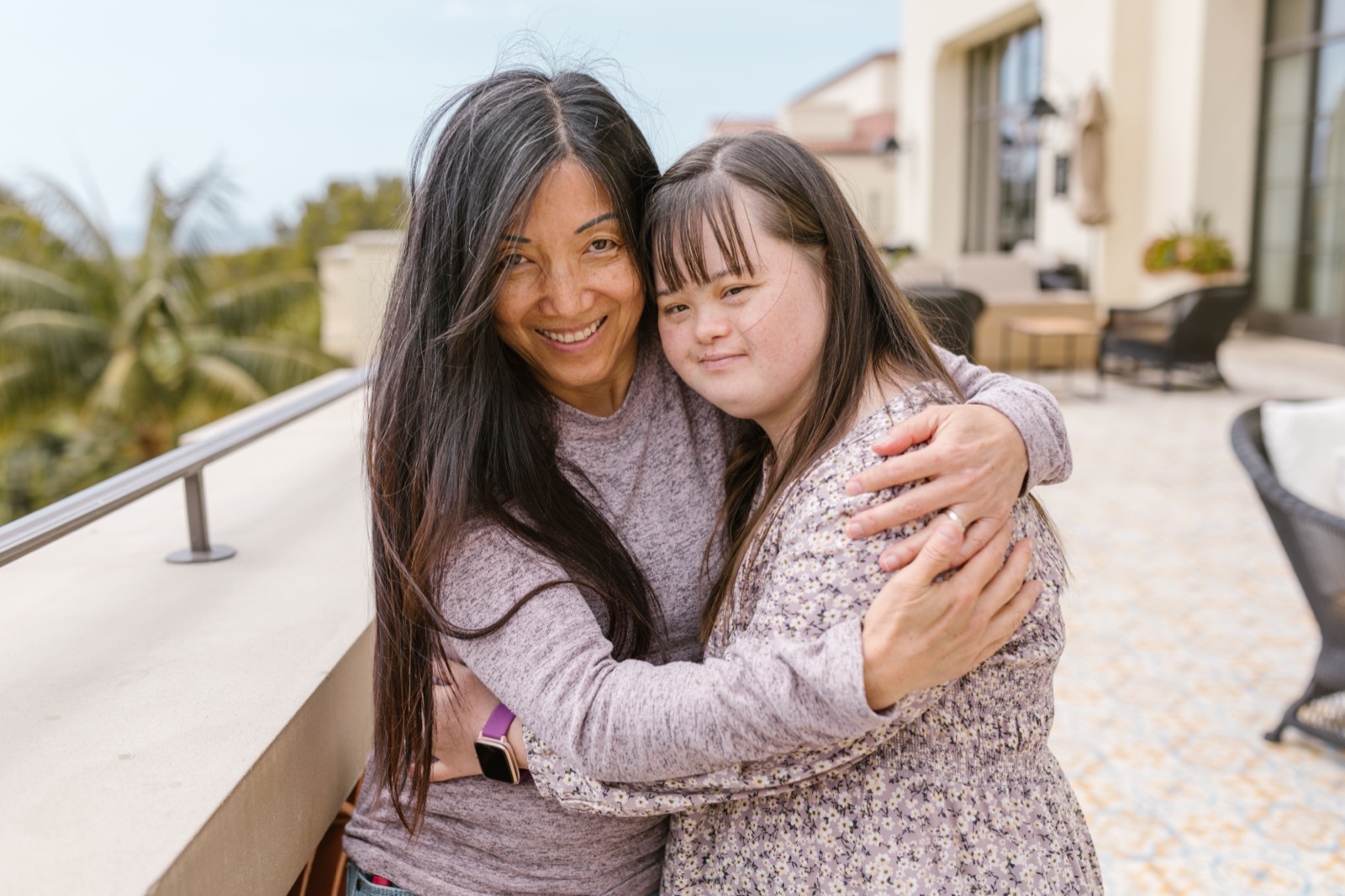 A mother embracing her adult daughter, who has Down syndrome, both smiling outdoors